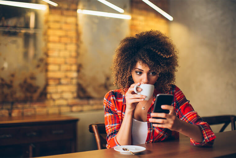 Young woman at cafe drinking coffee and using mobile banking app.