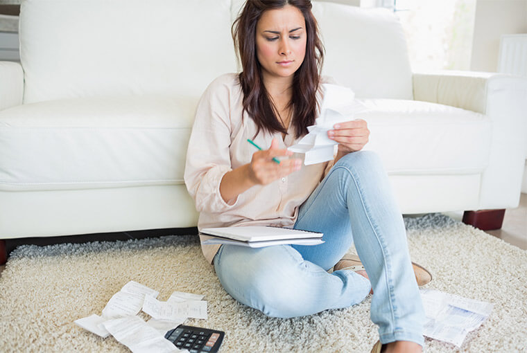 Woman sitting on floor adding up her bills