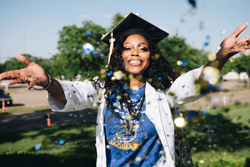 Woman wearing mortarboard celebrates graduation by throwing confetti in the air.