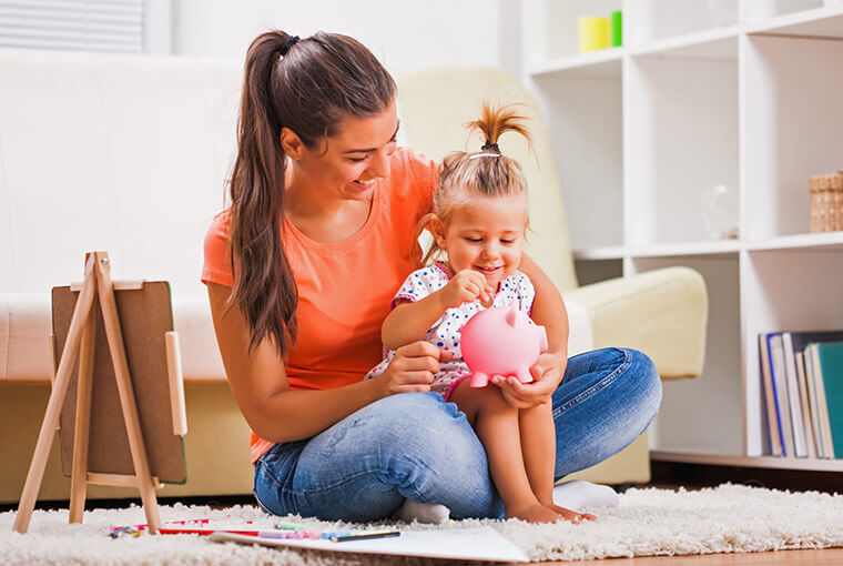 Mother with young daughter deposits coin in a piggy bank