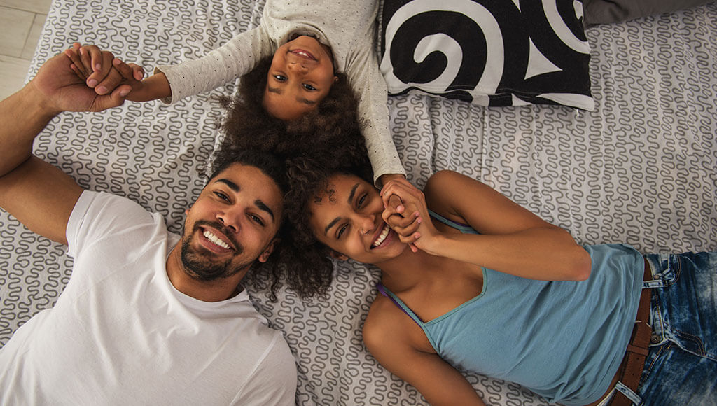 Smiling parents with daughter laying on backs looking up.