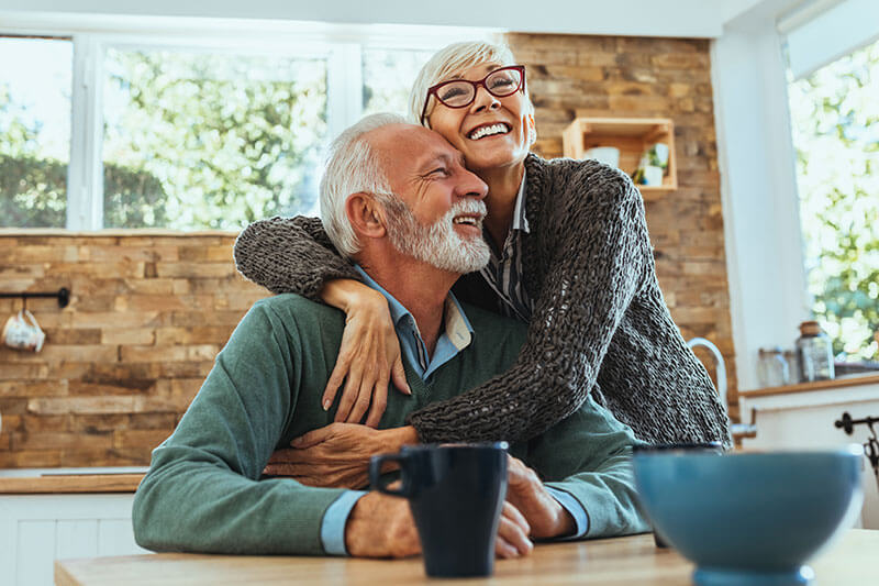 Woman hugging her husband at the breakfast table.