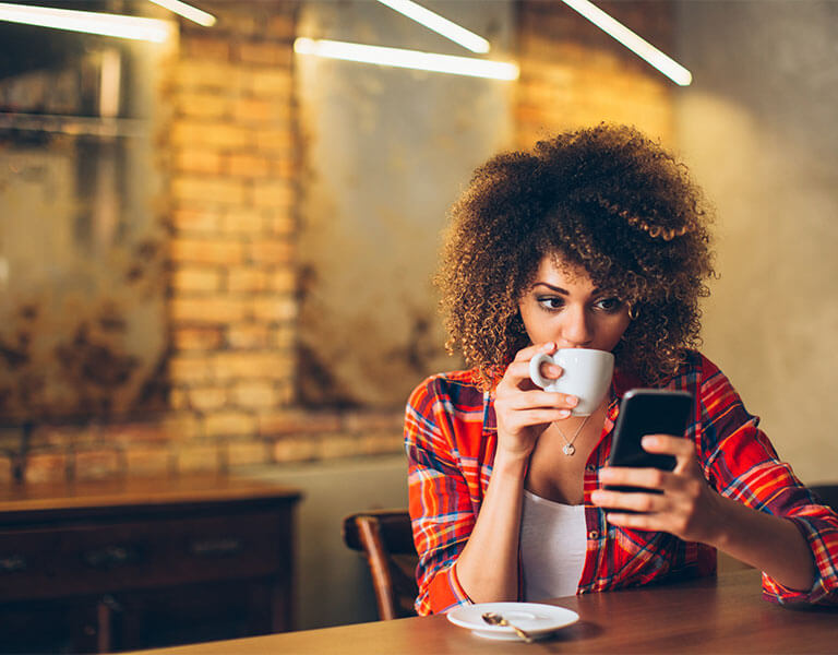Young woman at cafe drinking coffee and using mobile phone.