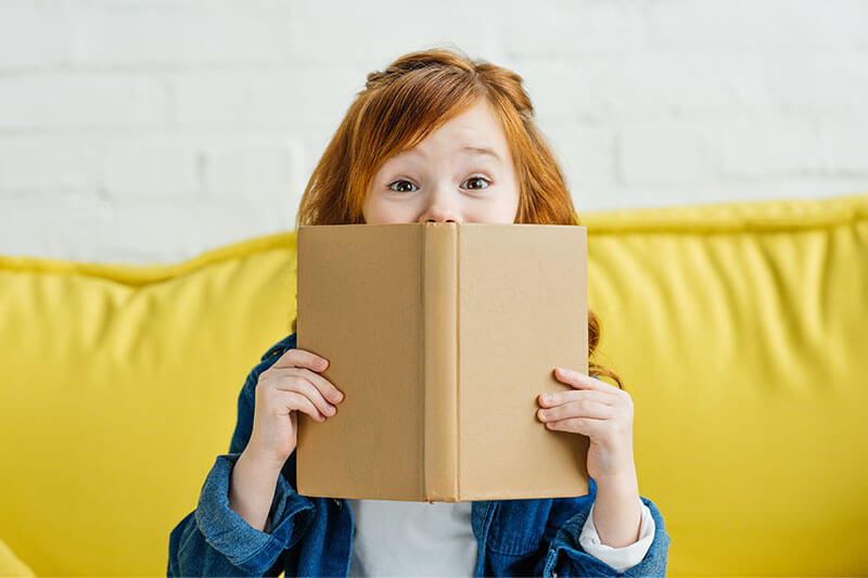 Little girl looking up from book in surprise.