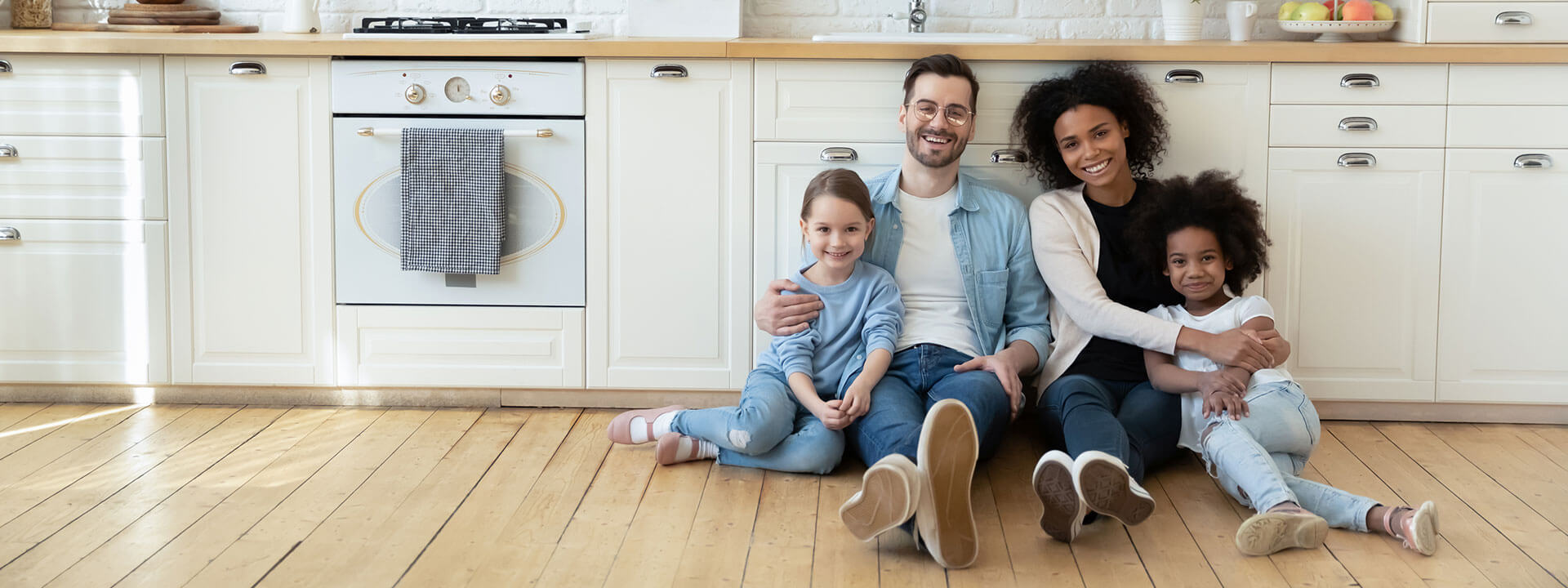 Happy young family with little kids sit on warm floor in their remodeled kitchen.