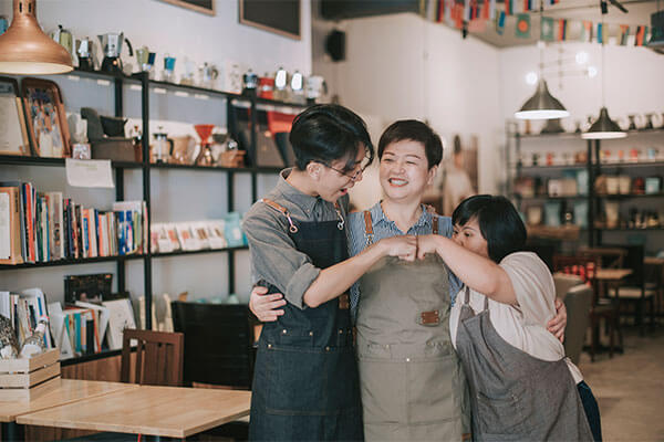 Two cafe employees and owner fist bump bonding together in cafe happily.