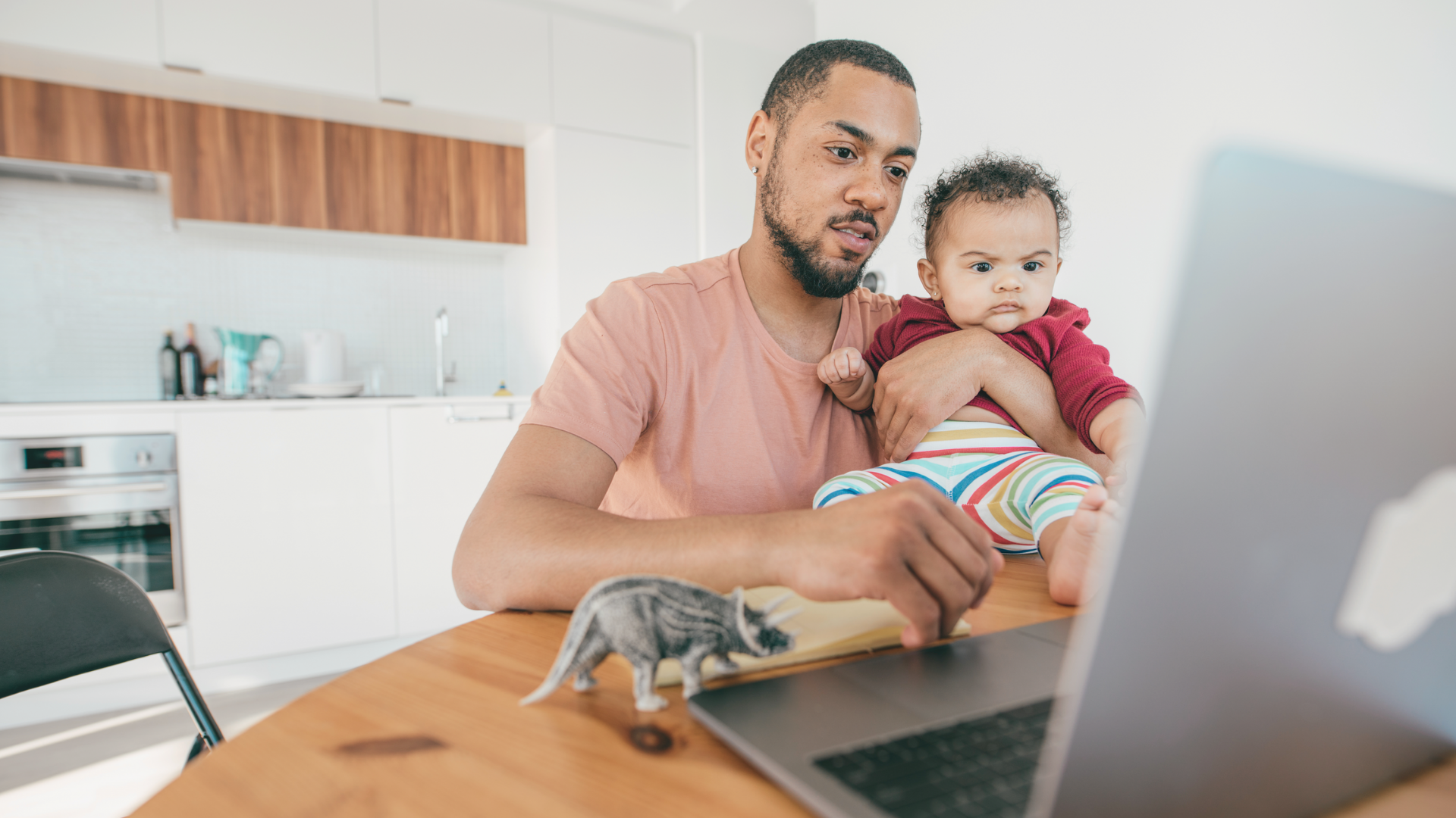Image of a man holding a baby sitting at a table with a lap top open indicating that he is using the Bill Pay eService from Prospera Credit Union. The image represents the convenience and ease of managing bills online and how the service can simplify your life.